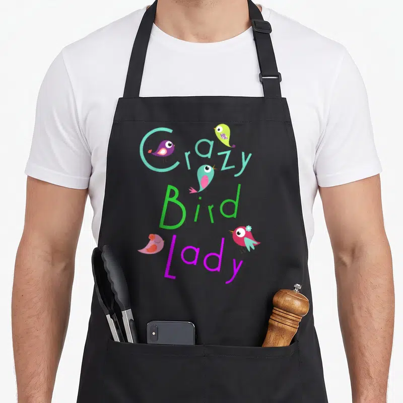 Funny pet bird apron - Crazy Bird Lady text with four colorful cartoon birds and a blue flower accent — shown on a black cotton canvas apron against a white background
