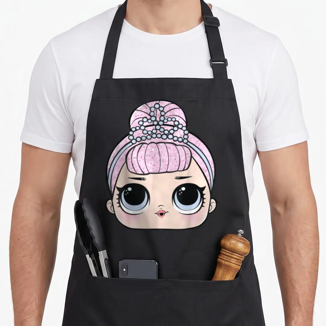 Lol face apron - Cartoon doll head with pink glitter hair, light blue tiara, peach skin, and large black eyes — shown on a black cotton canvas apron against a white background