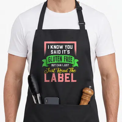 Gluten free celiac awareness apron - Stacked pink green and yellow text reading I know you said gluten free read — shown on a black cotton canvas apron against a white background
