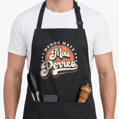 Dance modern apron - Retro orange circle with MENOS HATE Mas Perreo text in off-white and black script — shown on a black cotton canvas apron against a white background