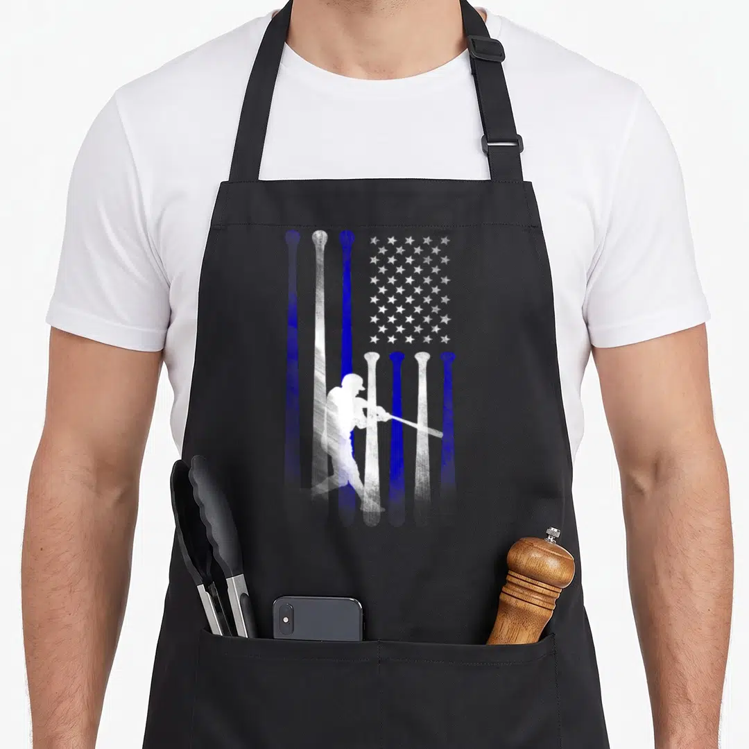 Player american flag apron - White baseball player silhouette over blue and white vertical bat stripes and star field — shown on a black cotton canvas apron against a white background