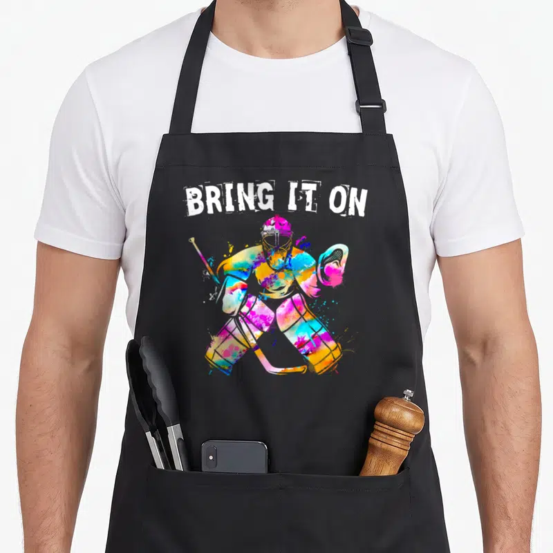 Goalie hockey ice apron - Watercolor hockey goalie in blue pink yellow cyan below arched white text BRING IT — shown on a black cotton canvas apron against a white background