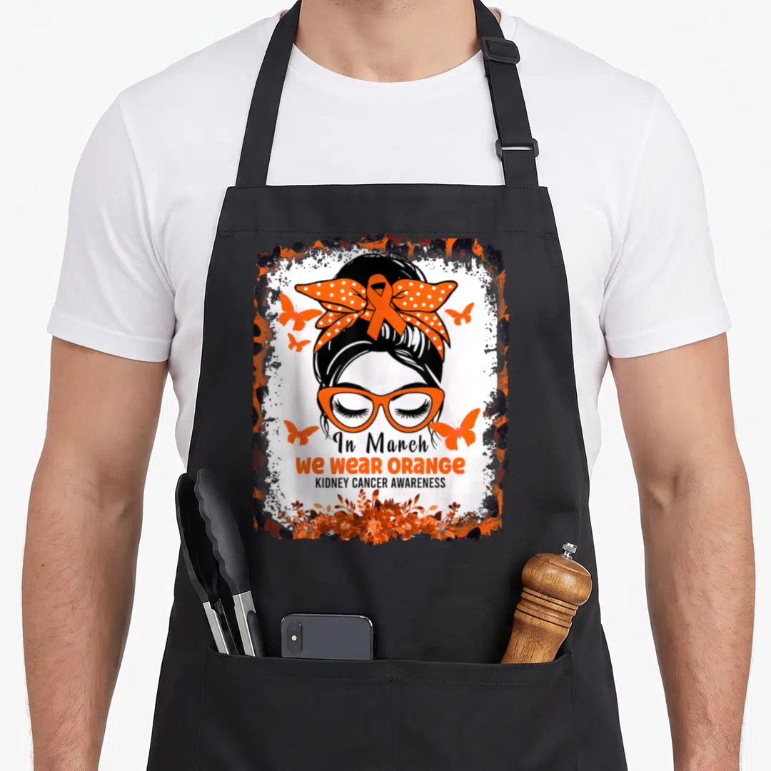 March messy aprons - Cartoon woman with glasses and orange ribbon bow surrounded by butterflies and flowers — shown on a black cotton canvas apron against a white background