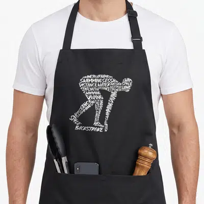 Sport swimming dad apron - White text forming swimmer silhouette with diving and backstroke phrases — shown on a black cotton canvas apron against a white background