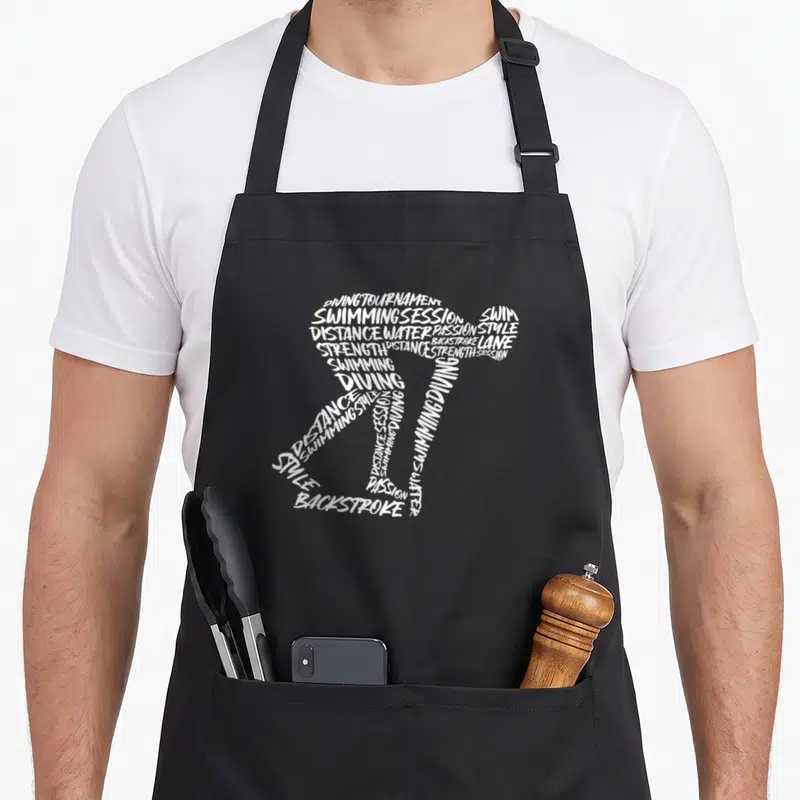 Sport swimming dad apron - White text forming swimmer silhouette with diving and backstroke phrases — shown on a black cotton canvas apron against a white background