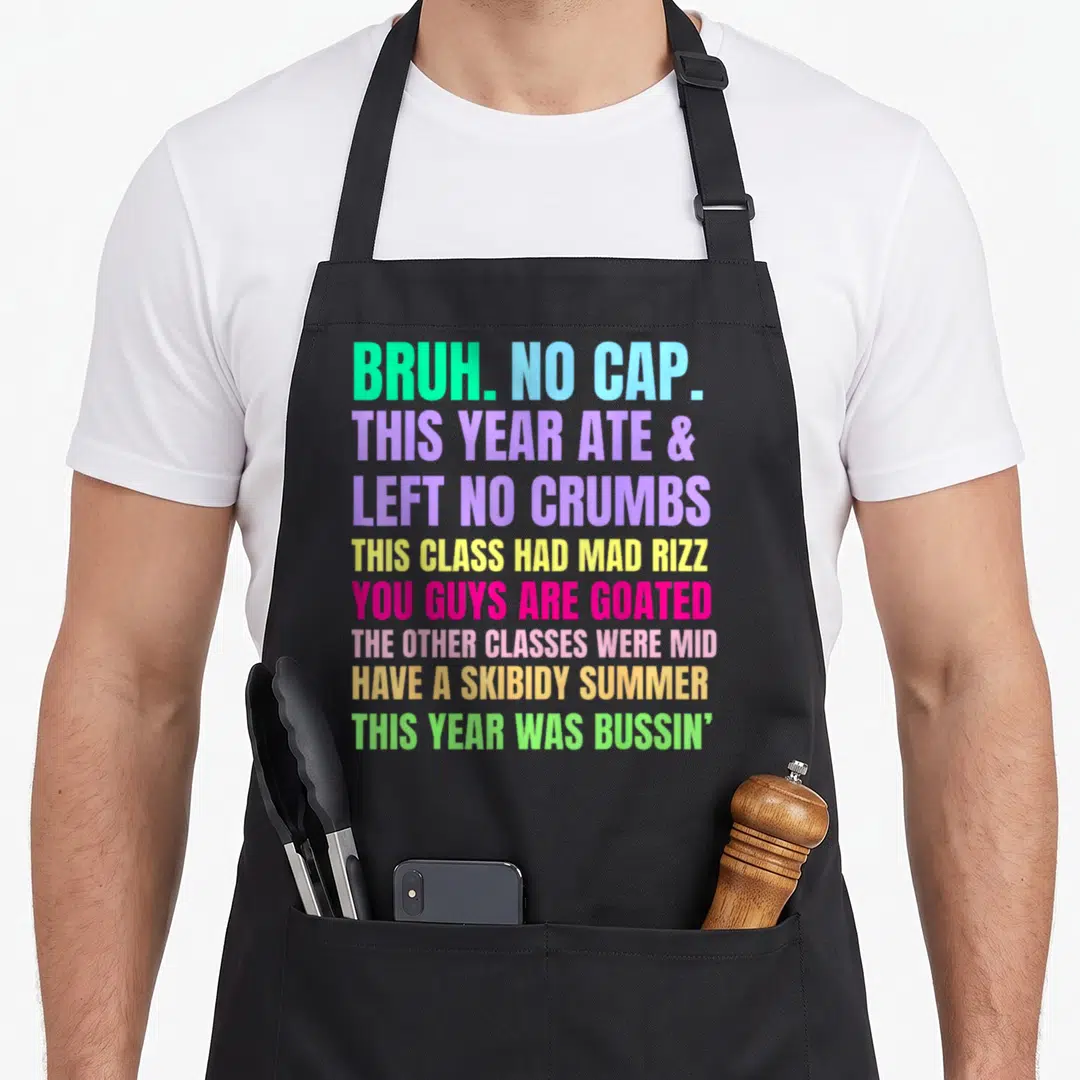 Gen teacher apron - Stacked colorful Gen Z slang text phrases including BRUH NO CAP and MAD RIZZ on grey background — shown on a black cotton canvas apron against a white background