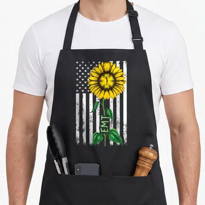 Hippie american flag apron - Sunflower with Star of Life center over distressed white flag with vertical EMT text — shown on a black cotton canvas apron against a white background