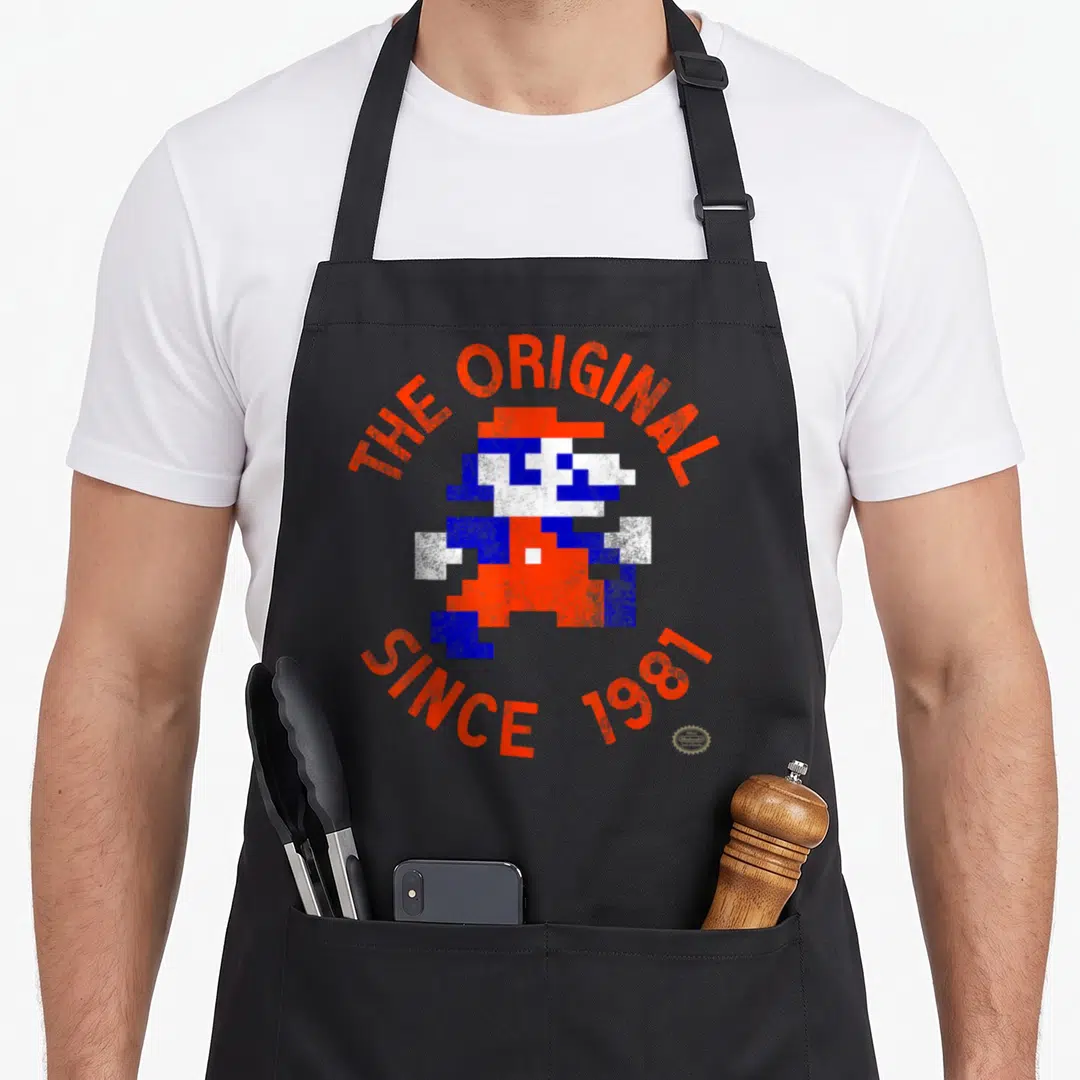 Bit original since birth apron - Pixel art character in orange blue white with arched text THE ORIGINAL SINCE 1981 — shown on a black cotton canvas apron against a white background
