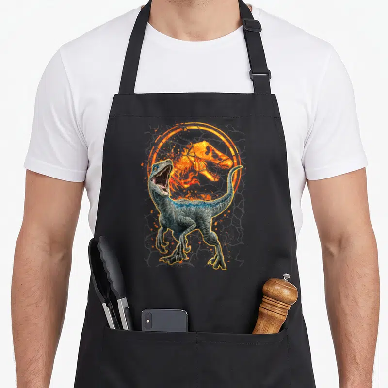 Blue prey love apron - Realistic blue velociraptor standing before orange t-rex skull inside circular magma ring — shown on a black cotton canvas apron against a white background
