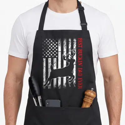 Buckin american flag apron - Grey deer silhouette over distressed flag with vertical red text — shown on a black cotton canvas apron against a white background