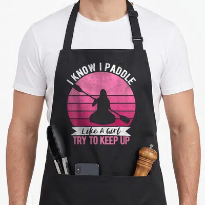 Paddling kayaking apron - Retro pink striped sun with grey paddler silhouette and text I KNOW I PADDLE Like A Girl TRY — shown on a black cotton canvas apron against a white background
