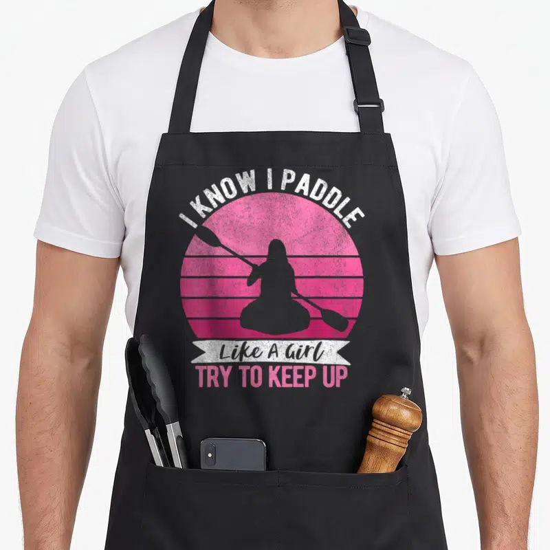 Paddling kayaking apron - Retro pink striped sun with grey paddler silhouette and text I KNOW I PADDLE Like A Girl TRY — shown on a black cotton canvas apron against a white background