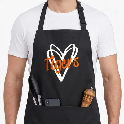 Tiger sports team aprons - White heart outline with orange Tigers script text on black fabric — shown on a black cotton canvas apron against a white background