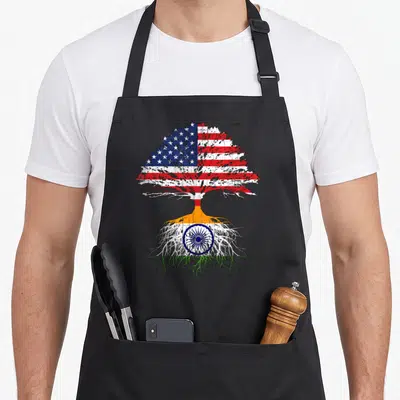 India indio apron - Tree with USA flag canopy and India flag roots in distressed colors — shown on a black cotton canvas apron against a white background