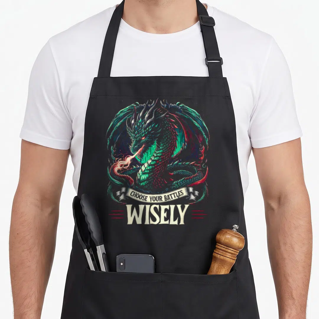 Rpg master apron - Realistic dragon breathing fire with banner text CHOOSE YOUR BATTLES WISELY below — shown on a black cotton canvas apron against a white background