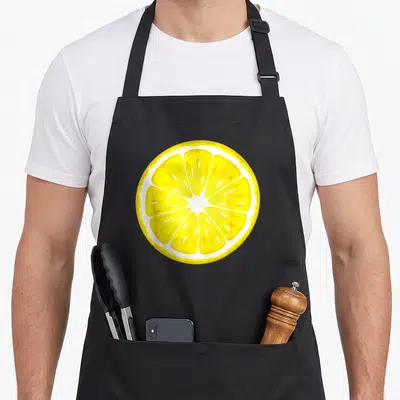 Costume lemon apron - Yellow and white cartoon lemon slice graphic on apron with two front pockets — shown on a black cotton canvas apron against a white background