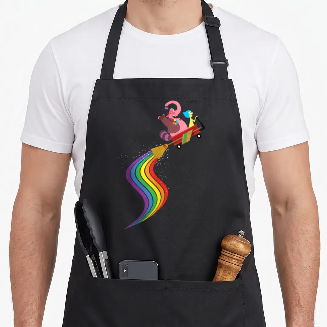Bing rainbow apron - Pink elephant and blue-haired girl in red wagon with rainbow broom trail — shown on a black cotton canvas apron against a white background