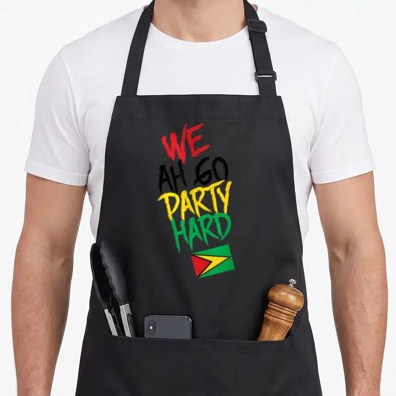 Hard guyanese apron - Stacked WE AH GO PARTY HARD text in red, black, yellow, green above small Guyana flag — shown on a black cotton canvas apron against a white background