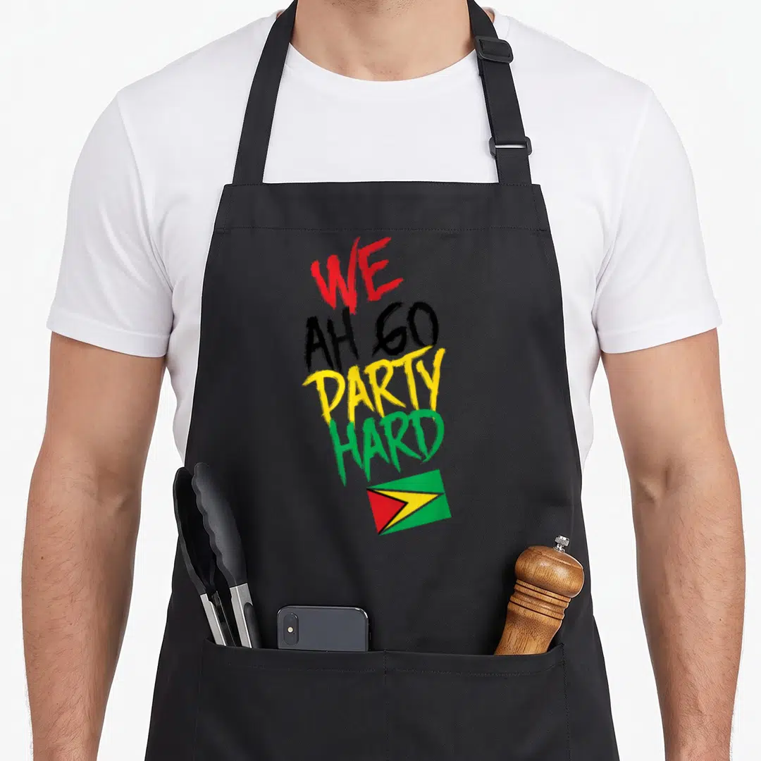 Hard guyanese apron - Stacked WE AH GO PARTY HARD text in red, black, yellow, green above small Guyana flag — shown on a black cotton canvas apron against a white background