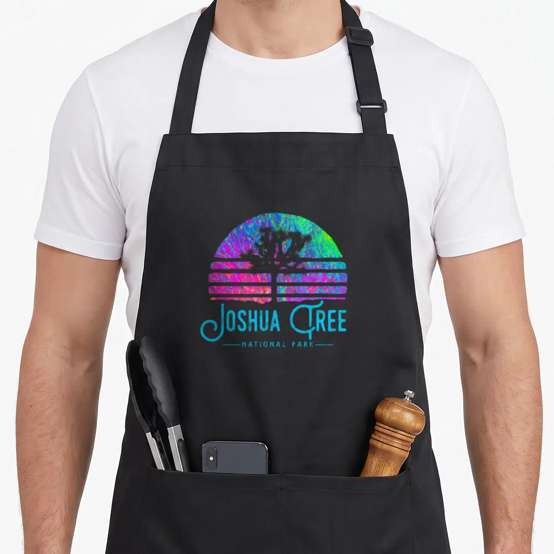 Psychedelic road apron - Retro psychedelic sun and landscape with JOSHUA TREE NATIONAL PARK text in blue pink green — shown on a black cotton canvas apron against a white background