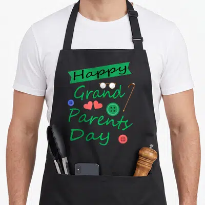 Grandparent generations apron - Happy Grand Parents Day text with glasses cane buttons and hearts in green red blue — shown on a black cotton canvas apron against a white background