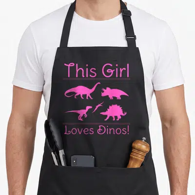 Funny dino dinosaur apron - Five pink dinosaur silhouettes separated by dotted lines from pink text on black — shown on a black cotton canvas apron against a white background