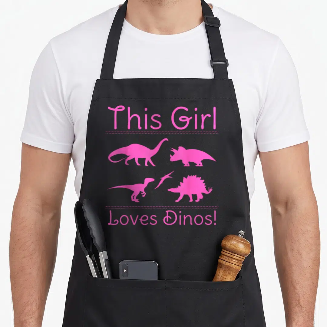 Funny dino dinosaur apron - Five pink dinosaur silhouettes separated by dotted lines from pink text on black — shown on a black cotton canvas apron against a white background