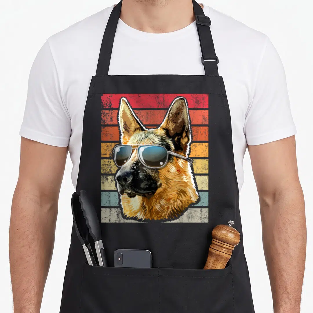 Cute german dog mom apron - Retro German Shepherd head wearing sunglasses against red orange and blue stripes — shown on a black cotton canvas apron against a white background