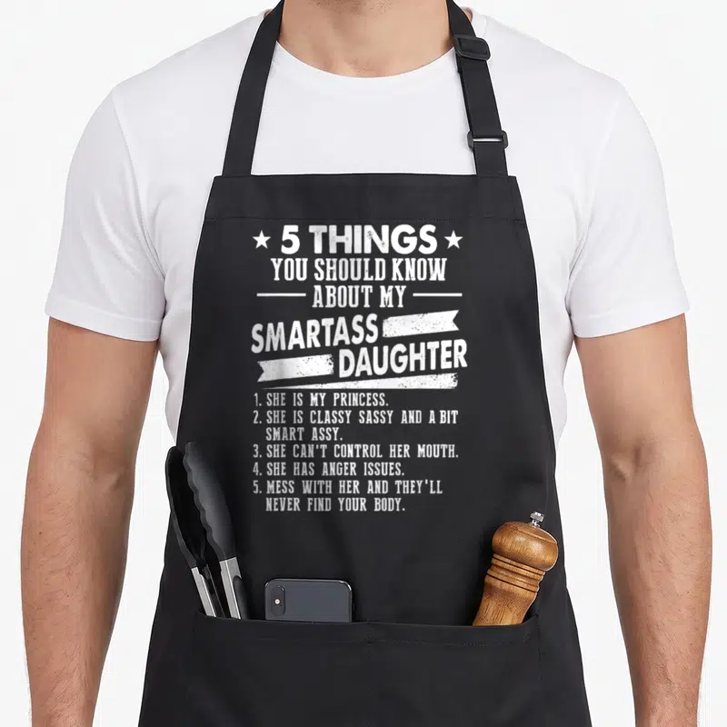 Should daddy daughter apron - White distressed text listing 5 things about a smartass daughter flanked by stars — shown on a black cotton canvas apron against a white background