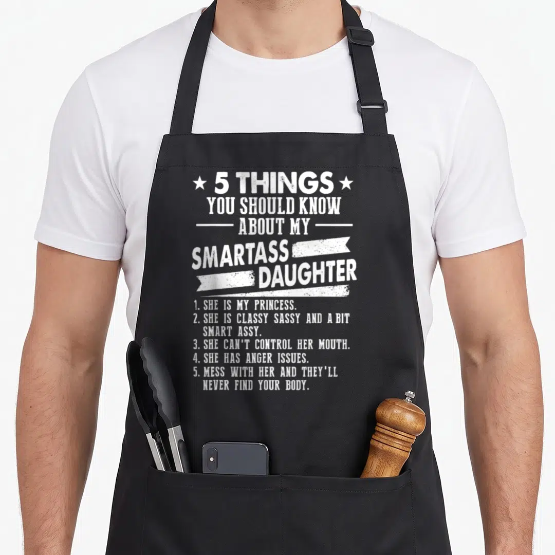 Should daddy daughter apron - White distressed text listing 5 things about a smartass daughter flanked by stars — shown on a black cotton canvas apron against a white background