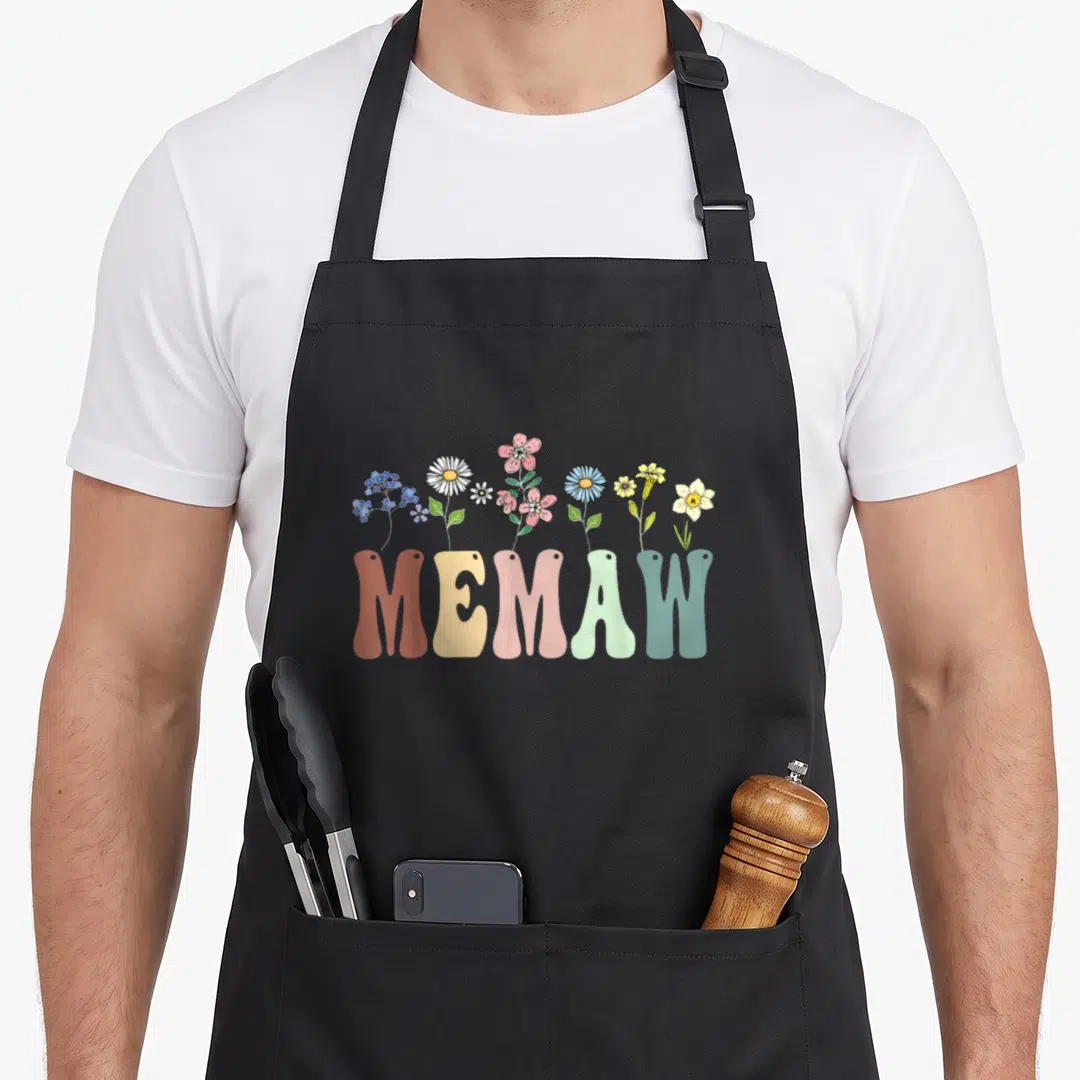 Memaw floral apron - Cartoon wildflowers in pink blue yellow green and orange growing from bold MEMAW letters — shown on a black cotton canvas apron against a white background