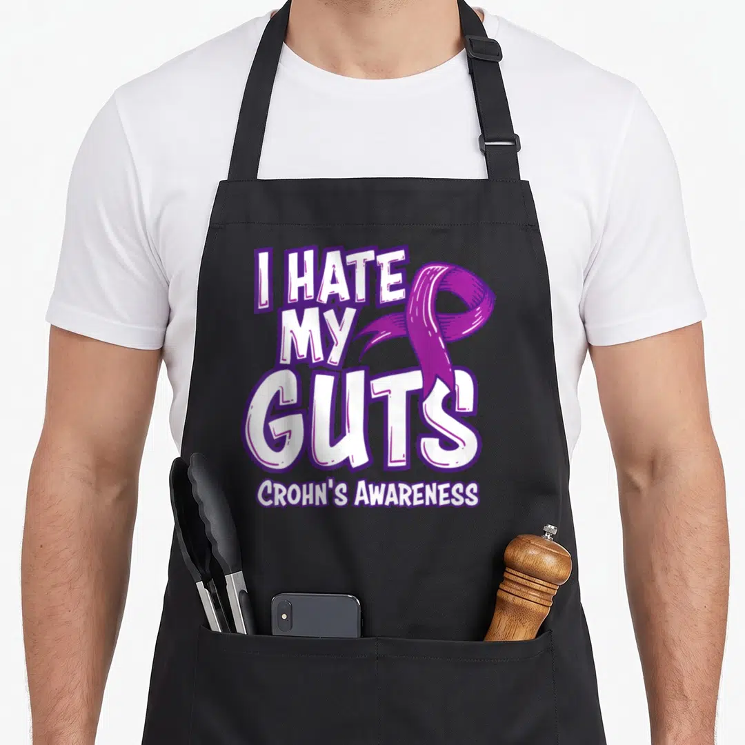 Gut ribbon apron - Purple ribbon and white text reading I HATE MY GUTS Crohn's Awareness — shown on a black cotton canvas apron against a white background