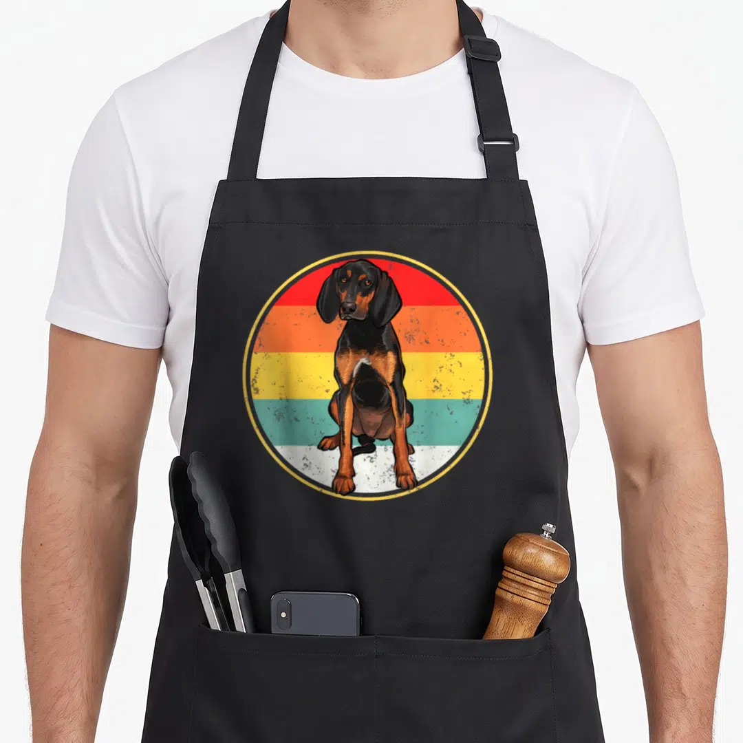 Sunset coonhound dog apron - Seated black and tan hound in front of circular retro sunset stripes — shown on a black cotton canvas apron against a white background