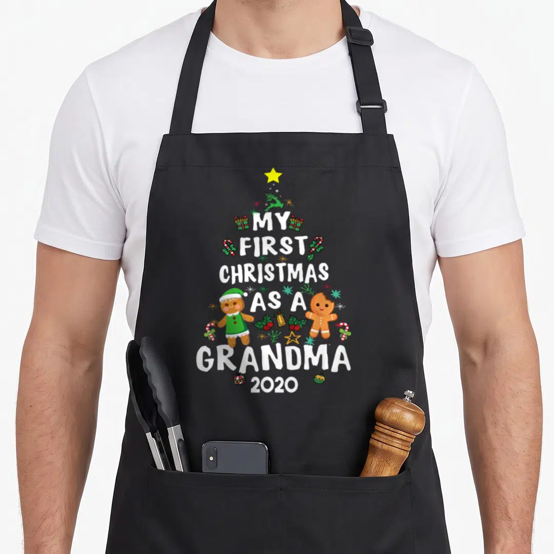 Grandma christmas aprons - Tree shape text My First Christmas As A Grandma 2020 with gingerbread and star — shown on a black cotton canvas apron against a white background