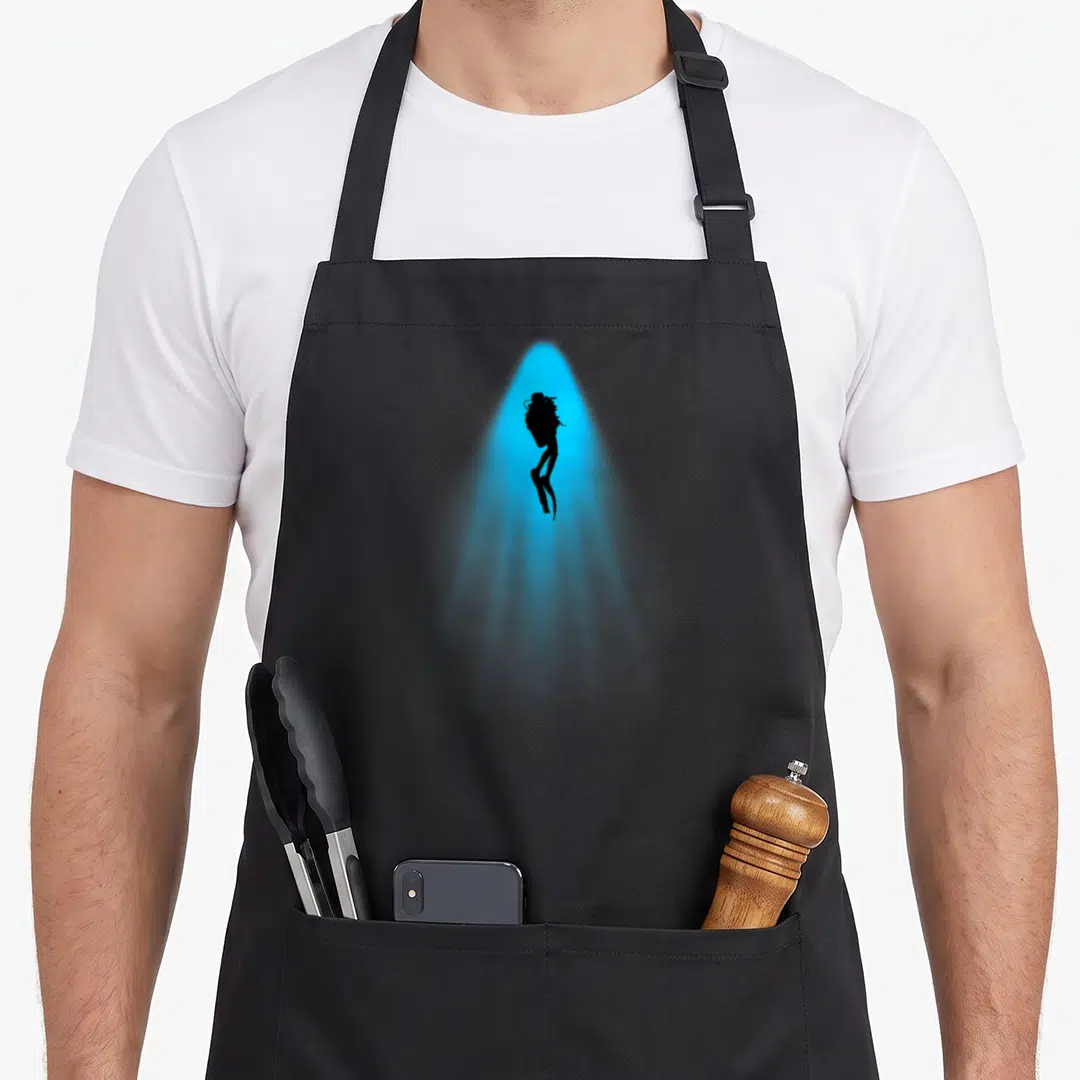 Ocean diving apron - Black silhouette of a female diver inside a blue spotlight beam — shown on a black cotton canvas apron against a white background