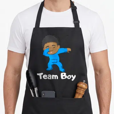 Gender dabbing boys apron - Cartoon baby in blue onesie dabbing with white Team Boy text underneath — shown on a black cotton canvas apron against a white background