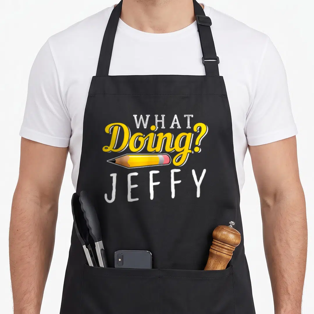 Jeffy novelty apron - What Doing Jeffy text with horizontal yellow pencil and white lettering — shown on a black cotton canvas apron against a white background