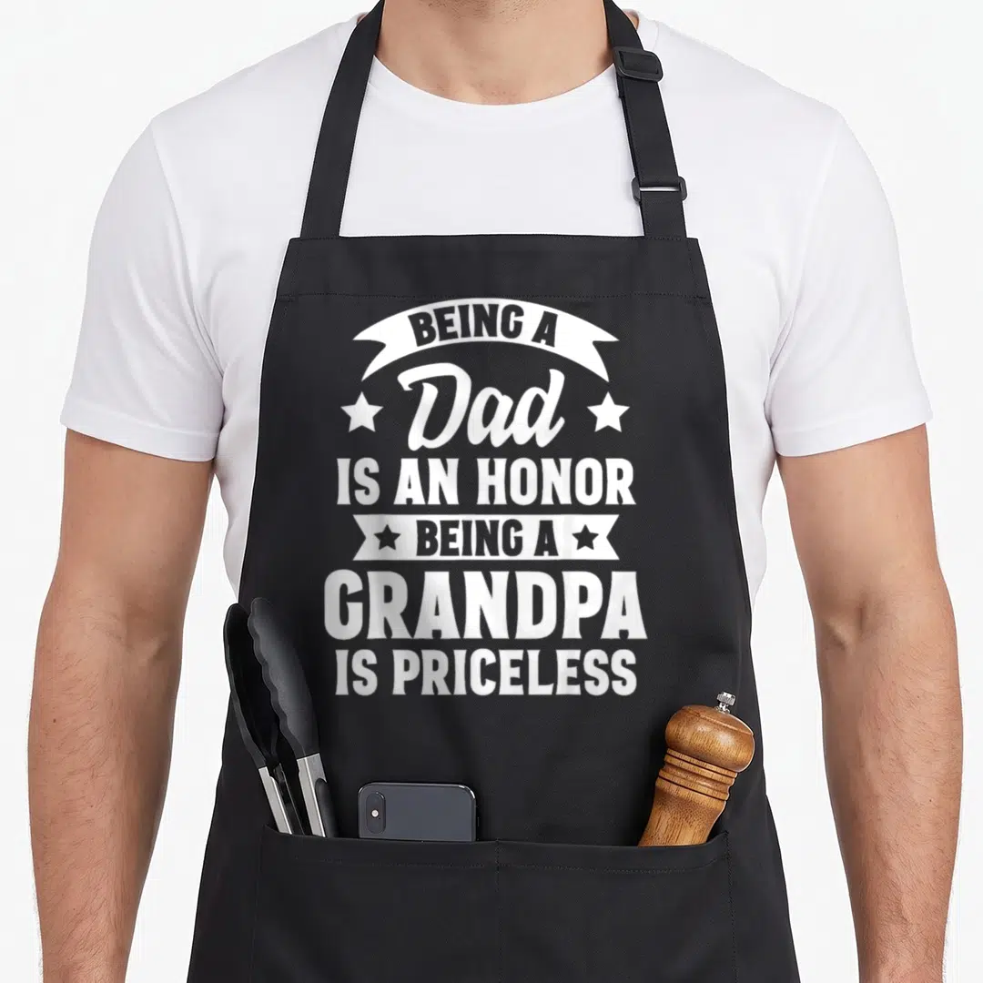 Honor priceless grandpa apron - White stacked text 'Being A Dad Is An Honor Being A Grandpa Is Priceless' on black — shown on a black cotton canvas apron against a white background
