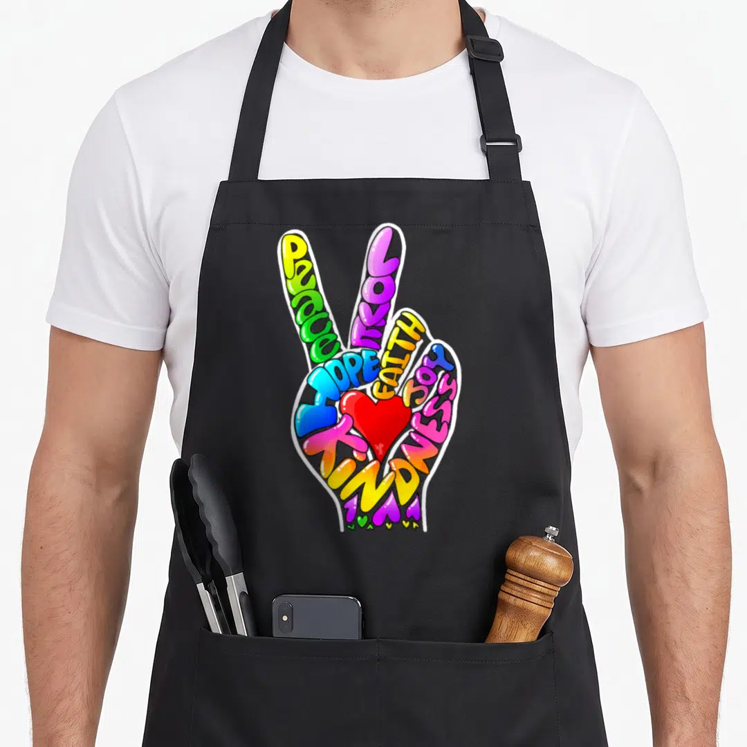 Peace faith aprons - Cartoon hand formed by words PEACE LOVE HOPE FAITH JOY KINDNESS with red heart and small hearts — shown on a black cotton canvas apron against a white background