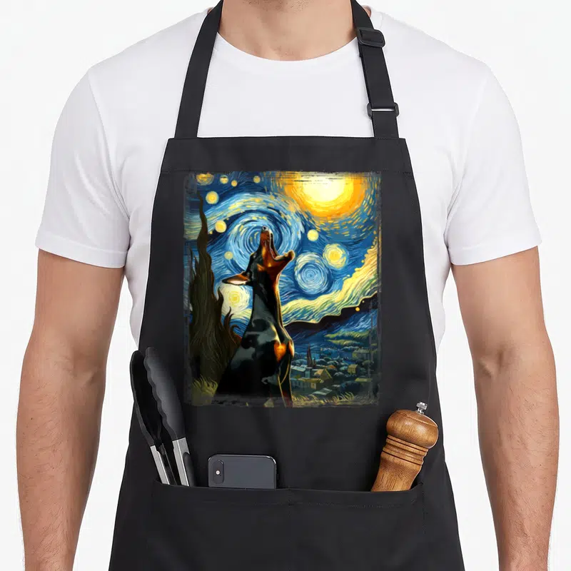 Doberman van gogh apron - Realistic black dog howling under a swirling blue and yellow starry night sky with a cypress — shown on a black cotton canvas apron against a white background