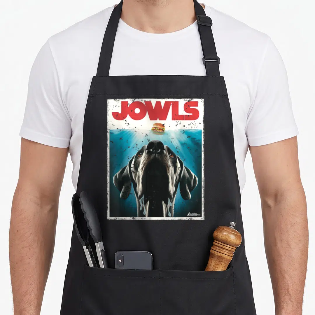 Monstermuttz dog apron - Red JOWLS text above black dog in blue water reaching for floating hamburger — shown on a black cotton canvas apron against a white background