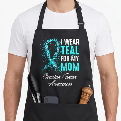 Ovarian mother's apron - Teal heart ribbon and stacked text I wear teal for my mom ovarian cancer awareness — shown on a black cotton canvas apron against a white background
