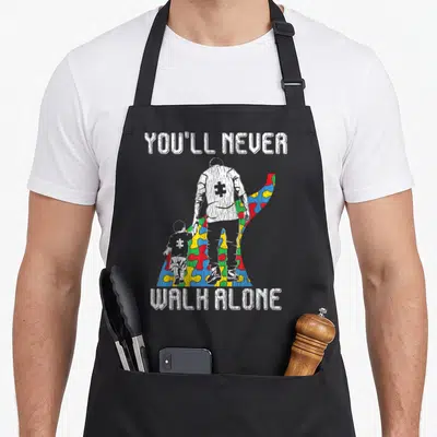 Family father son apron - Distressed man and child on red blue yellow green puzzle path with white text — shown on a black cotton canvas apron against a white background