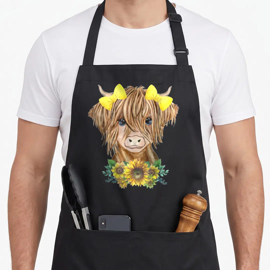 Funny sunflower highland cow apron - Watercolor brown highland cow with two yellow bows and yellow sunflowers — shown on a black cotton canvas apron against a white background
