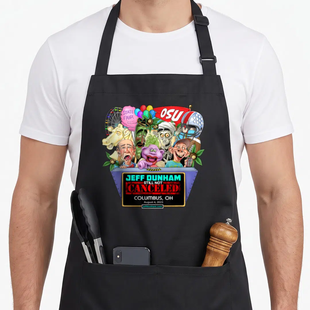 Jeff dunham hollywood apron - Puppets clustered behind blue stage with OSU banner and gold plaque reading still not — shown on a black cotton canvas apron against a white background