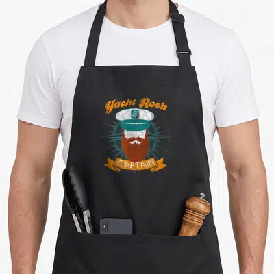 Yacht boat apron - Retro captain hat and beard with Yacht Rock arched text and CAPTAIN ribbon — shown on a black cotton canvas apron against a white background