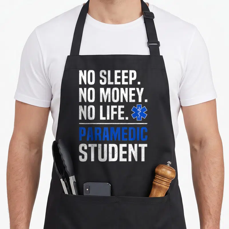 Sleep money apron - NO SLEEP NO MONEY NO LIFE PARAMEDIC STUDENT text with blue Star of Life symbol — shown on a black cotton canvas apron against a white background