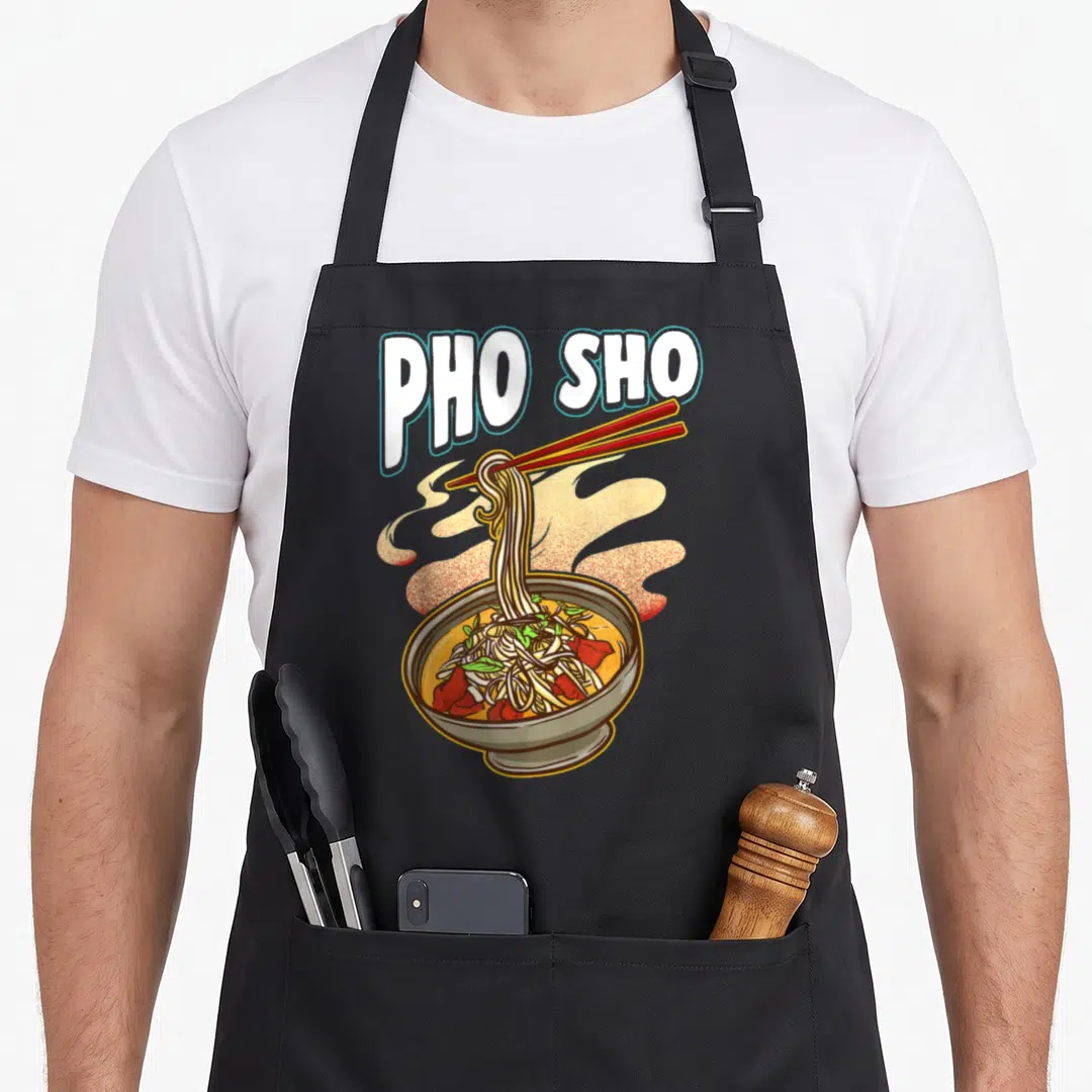 Rice pho apron - PHO SHO text above cartoon bowl of noodles lifted by red chopsticks with steam — shown on a black cotton canvas apron against a white background
