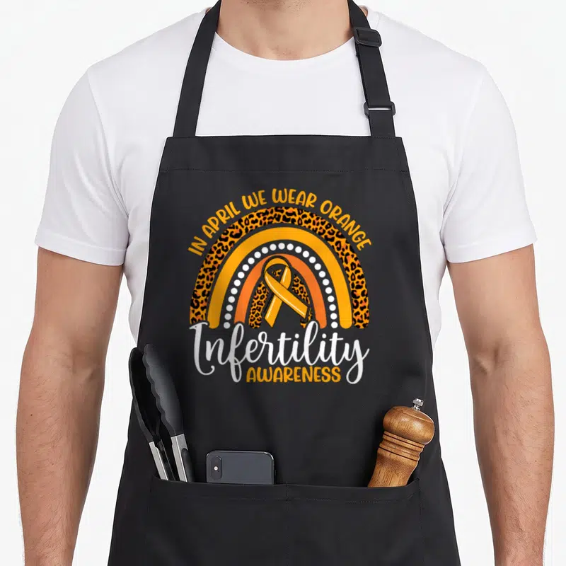 Week rainbow apron - Leopard print rainbow with orange ribbon and Infertility Awareness text — shown on a black cotton canvas apron against a white background
