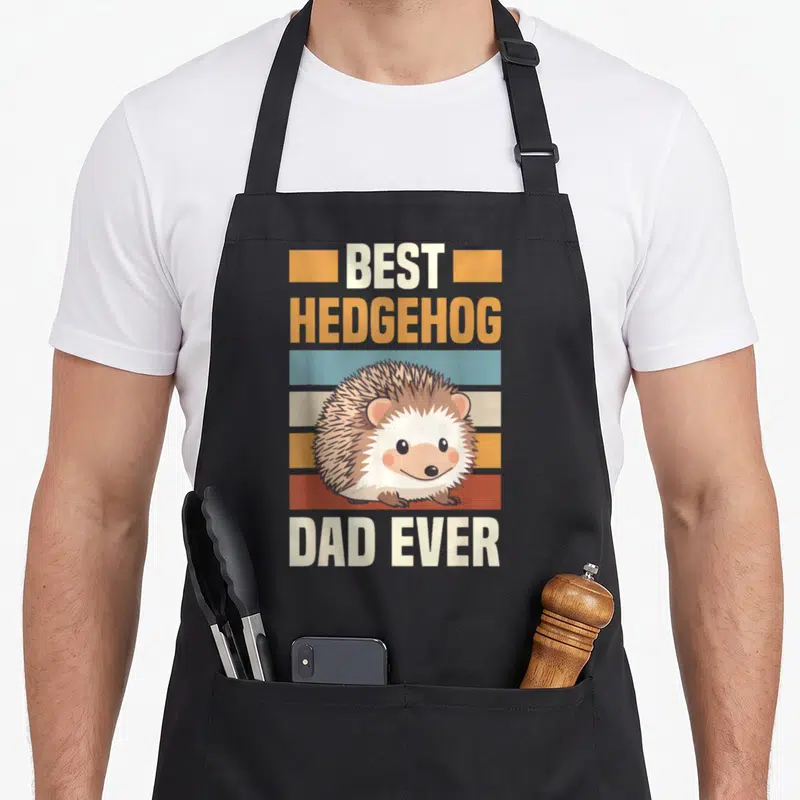 Prickly animal apron - Cartoon hedgehog over orange blue red stripes with best hedgehog dad ever text — shown on a black cotton canvas apron against a white background